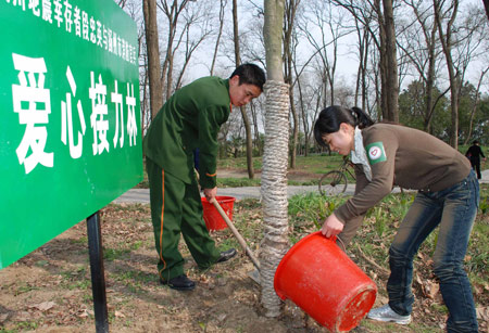 Duan Zhongying (R), a survivor of last year's Sichuan earthquake, plants a tree with Hu Shuiming, one of the firemen who rescued her, in Yangzhou, east China's Jiangsu Province, March 17, 2009. [Wang Zhuo/Xinhua]