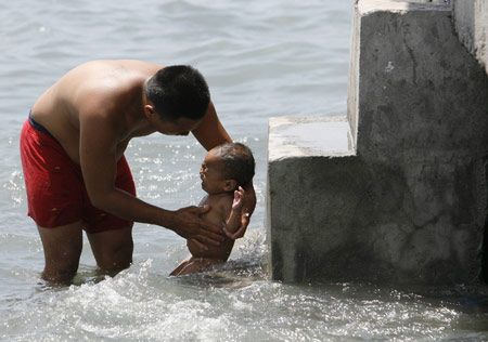 A father bathes his son to beat the simmering heat in polluted Manila bay March 18, 2009. The summer season officially started on the last week of February and is expected to end around the second week of May. [Xinhua/Reuters] 