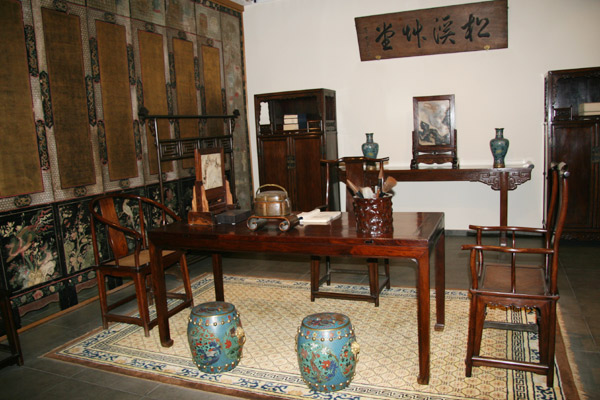 A room arranged with furnishings modelled on traditional Chinese family style: the study of Huanghuali furniture. The four chairs placed around the table show the status of people sitting on them. The highest ranking person sits on the chair behind the table, and the lowest ranking person sits on the stools in front of the table.
