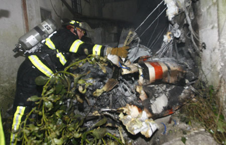 A fire fighter looks at parts of a crushed plane in the backyard of a building after a plane crushed on its roof in Quito March 19, 2009.[Xinhua/Reuters]