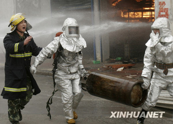  Firefighters carry out tanks of liquid gas out of a burning gas tank warehouse in downtown Luoyang, central China's Henan province, March 21, 2009. [Xinhua]