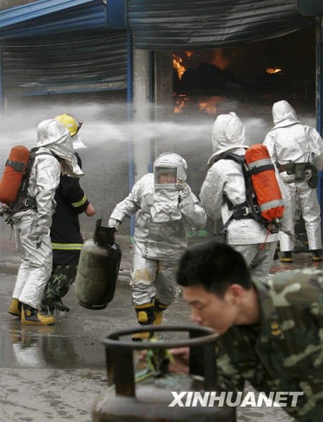  Firefighters carry out tanks of liquid gas out of a burning gas tank warehouse in downtown Luoyang, central China's Henan province, March 21, 2009. [Xinhua]