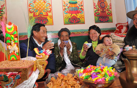 An elderly woman (C) who used to be a serf in Old Tibet drinks buttered tea with her family and Norxi (1st L), an official from local Tibet government who came to visit her at her house in a village in Qamdo, southwest China's Tibet Autonomous Region, March 22, 2009. [Xinhua photo]
