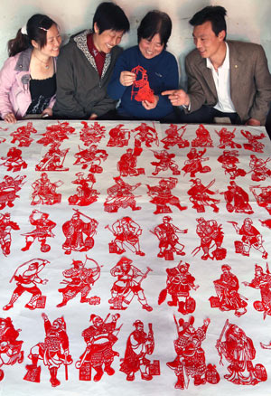Folk artist Wang Zhenzhu (2nd R) shares pleasure with neighbors in appreciating her paper-cuttings of 108 generals of Chinese classic novel 'Outlaws of the Marsh', in Yuncheng, north China's Shanxi Province, March 24, 2009. It took Wang Zhenzhu some three months to finish the vivid paper-cuttings of aesthetic value. [Xue Jun/Xinhua]