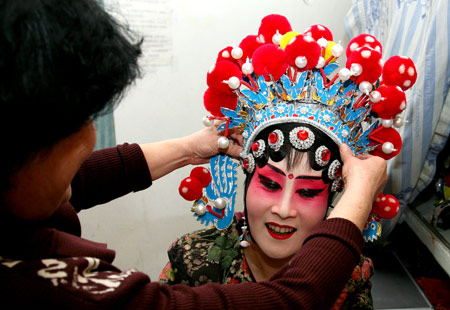 An actress of the Qin Opera Art Troupe of Hami puts on head decoration before getting on stage in a theater of Hami, northwest China's Xinjiang Uygur Autonomous Region, March 18, 2009. [Cai Zengle/Xinhua]