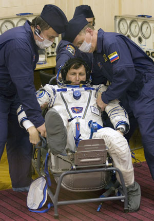 Ground personnel assist U.S. entrepreneur Charles Simonyi (C) to get up after he put on his space suit at Baikonur Cosmodrome March 26, 2009.[Xinhua/Reuters]