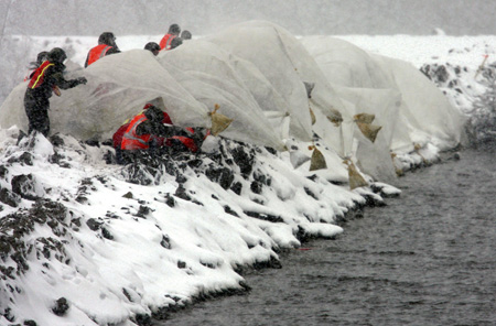 U.S. Army National Guard soldiers launch a large sheet of plastic with sandbag weights over the side of an earthen dike on the southside of Fargo, North Dakota March 30, 2009.