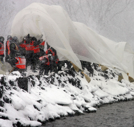 U.S. Army National Guard soldiers launch a large sheet of plastic with sandbag weights over the side of an earthen dike on the southside of Fargo, North Dakota March 30, 2009.