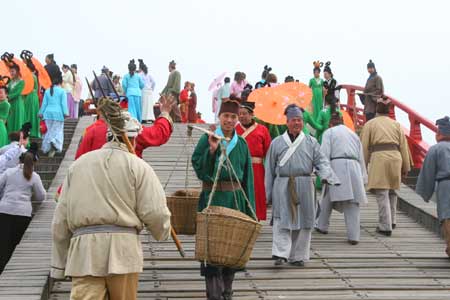 Chinese people in traditional costumes walk along a bridge to showcase the life of China's Northern Song Dynasty (960-1126 A.D.) at a tourism promotional initiative during the Qingming festival, or the Tomb-sweeping Day, in Kaifeng city, central China's Henan Province, April 4, 2009. Local organizers and working staff copied the thriving life of the ancient city of Kaifeng, then capital of the Northern Song Dynasty, aiming to attract more tourists. [Xinhua]