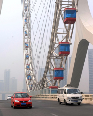 Vehicles roll past under an observation wheel newly-built as a landmark scenery in north China's coastal city of Tianjin, April 5, 2009. The brand-new observation wheel, which is to operate on April 28, is 110 meters in diameter and costs 30 minutes for one circle. [Xinhua]