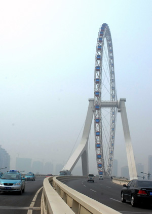 Vehicles roll past under an observation wheel newly-built as a landmark scenery in north China's coastal city of Tianjin, April 5, 2009. The brand-new observation wheel, which is to operate on April 28, is 110 meters in diameter and costs 30 minutes for one circle. [Xinhua]