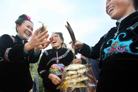 A bevy of ethnic Miao women laugh at taking living fish as gift for the fiesta of the Guzang (to bury the drum) Festival, at the Yangfang Village, Taijiang County, southwest China's Guizhou Province, April 8, 2009. 