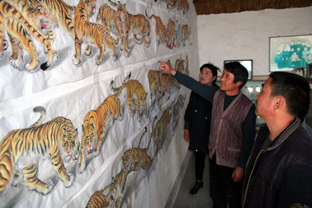 Wang Demin, a farmer fond of painting, introduces his tiger paintings to his fellow villagers at home in Tancheng County of east China's Shandong Province, April 8, 2009. Wang started to paint tigers this January and has finished 68 pieces of tiger pictures as he planed to make a hundred pieces before China's National Day on this Oct. 1st. (Xinhua/Zhang Chunlei)