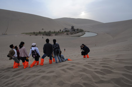 A tourist takes a photo for his companions near 'Crescent Moon Spring' in Dunhuang, northwest China's Gansu Province, on April 11, 2009. The tickets of all the scenic spots in Dunhuang, including the Mogao Grottoes, are offered at half price from March 1 to June 30 this year to promote tourism and ease the effect of global economic crisis. 