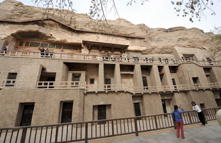 A tourist takes a photo for her companion in front of the Mogao Grottoes in Dunhuang, northwest China's Gansu Province, on April 11, 2009. 