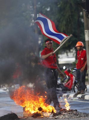 A supporter of former Thai Prime Minister Thaksin Shinawatra waves a national flag near burning tyres as protesters block a main road in Bangkok April 13, 2009. The Thai army cracked down on anti-government protesters on Monday, firing warning shots at a major junction in the capital at demonstrators who responded by hurling petrol bombs, witnesses said. [Xinhua/Reuters] 