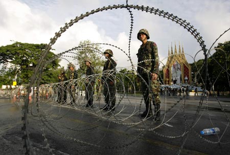 Soldiers stand behind a wire barricade during a gathering of supporters of former Thai Prime Minister Thaksin Shinawatra in Bangkok April 13, 2009. The Thai army cracked down on anti-government protesters on Monday, firing warning shots at a major junction in the capital at demonstrators who responded by hurling petrol bombs, witnesses said. [Xinhua/Reuters]