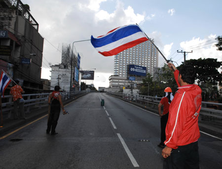 An anti-government protester waves the national flag at the Din Daeng intersection in Bangkok, capital of Thailand, on April 13, 2009. At least 77 were wounded when hundreds of army soldiers and anti-government protesters clashed in Bangkok early Monday morning, Thai media reports.[Thana Nuntavoranut/Xinhua]