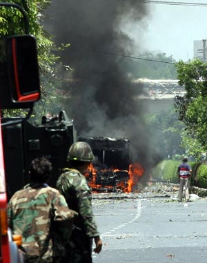 Thai soldiers look at a burning vehicle near the Government House in Bangkok, capital of Thailand, April 14, 2009. Thai anti-government protesters began to head home Tuesday afternoon after their leaders surrendered to police and called an end to the rally. But the security in the capital Bangkok is still tight. [Zhang Fengguo/Xinhua]