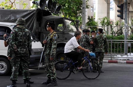 A man rides past army soldiers near the royal Chiralada Palace in Bangkok, capital of Thailand, April 14, 2009. Thai anti-government protesters began to head home Tuesday afternoon after their leaders surrendered to police and called an end to the rally. But the security in the capital Bangkok is still tight. [Huang Haimin/Xinhua]