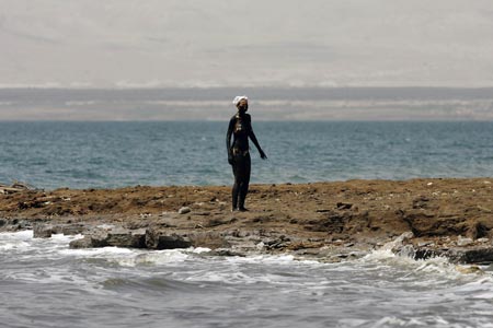 A tourist covered with black mud walks on Jordan's side of the Dead Sea, the lowest point on earth, April 15, 2009. A growing number of medical patients and visitors are flocking to Jordan's Dead Sea for its black mud, which is thought to possess healing properties that can treat skin diseases. [Xinhua/Reuters]