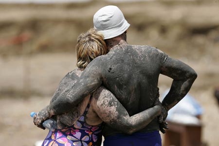 Tourists covered with black mud embrace on Jordan's side of the Dead Sea, the lowest point on earth, April 15, 2009. A growing number of medical patients and visitors are flocking to Jordan's Dead Sea for its black mud, which is thought to possess healing properties that can treat skin diseases. [Xinhua/Reuters]