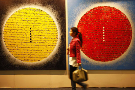 A visitor passes paintings during the opening day of the China International Gallery Exposition (CIGE) 2009 in Beijing April 15, 2009. The fair showcases over 80 selected galleries and presents some 5,000 pieces of art projects including painting, sculptures, multimedia creations.[Li Mingfang/Xinhua]