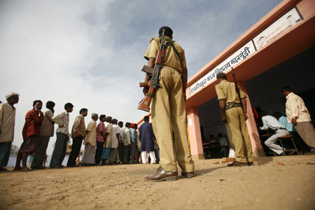 Voters line up to cast their votes as security personnel stand guard at a polling booth in Madangundi village, about 150 km (93 miles) north of the eastern Indian city of Ranchi April 16, 2009.