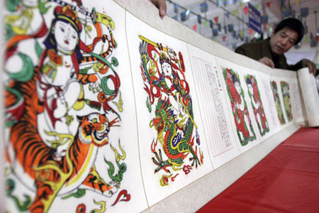 An exhibitor from Kaifeng City displays a 28-meter-long scroll of New Year Paintings at Henan Tourist Commodities Exposition in Sanmenxia, a city of central China's Henan Province, April 16, 2009. About 600 companies participated in the exposition with over 2,000 types of commodities on show including Luoyang Tri-colored Pottery of Tang Dynasty, embroidery of ancient Kaifeng, etc. [Xinhua/Zhang Xiaoli]