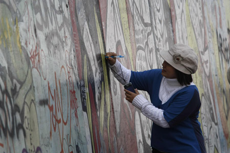 A woman writes on part of the former Berlin wall April 17, 2009. Artists this week began repainting the largest remaining section of Berlin Wall with the murals they created after the fall of the hated symbol of the Cold War almost 20 years ago. A 1,300 metre (4,265 ft) stretch of wall, the world&apos;s longest open-air art gallery, was decorated by 118 artists from 21 countries in 1990, but has since been damaged by the weather, exhaust fumes, vandals, and souvenir-seeking tourists. The restoration work is expected to be completed in time for the 20-year anniversary in November of the fall of the wall which once divided communist East Berlin from capitalist west Berlin. (Xinhua/Reuters Photo)