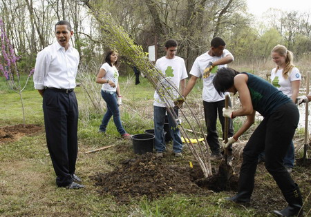 US President Barack Obama watches as first lady Michelle Obama (R) plants a Earth Day tree at Kenilworth Aquatic Gardens in Washington, April 21, 2009. [China Daily/Agencies]