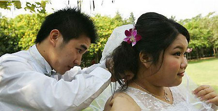 A man helps his fiancée adjust her wedding dress at a group engagement ceremony for nine obese girls in Guangzhou, capital of south China's Guangdong province on April 21, 2009. [sohu.com]