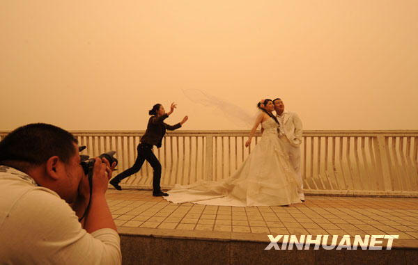 The photo taken on April 23, 2009 shows sandstorm hitting parts of Gansu Province, northwest China, April 23, 2009. A couple takes wedding photo in this photo. [Xinhua] 