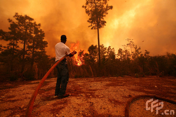 A man sprays water on a raging fire as it threatens nearby homes on April 23, 2009 near Conway, South Carolina. South Carolina Gov. Mark Sanford declared a state of emergency Thursday for a coastal county where a wildfire has consumed thousands of acres and destroyed dozens of homes. [Logan Mock-Bunting/GettyNorthAmerica/CFP]