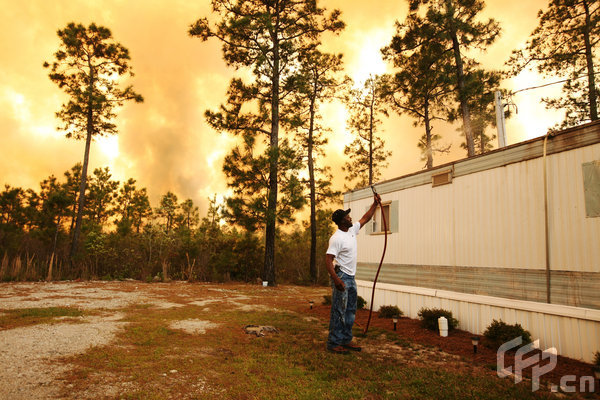 Scott Vereen sprays water on his family's home as a wildfire rages nearby on April 23, 2009 near Conway, South Carolina. South Carolina Gov. Mark Sanford declared a state of emergency Thursday for a coastal county where a wildfire has consumed thousands of acres and destroyed dozens of homes.[Logan Mock-Bunting/GettyNorthAmerica/CFP]