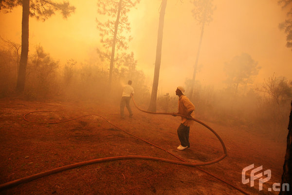 Two men spray water on a raging wildfire as it threatens nearby homes on April 23, 2009 near Conway, South Carolina. South Carolina Gov. Mark Sanford declared a state of emergency Thursday for a coastal county where a wildfire has consumed thousands of acres and destroyed dozens of homes. [Logan Mock-Bunting/GettyNorthAmerica/CFP]