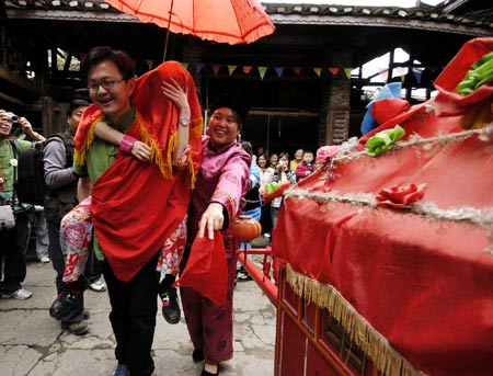 A tourist carries his girl friend who is dressed up as a bride by local villagers of Tujia ethnic group on the back as they experience the local marriage traditions at a tourist destination in Jiangkou County, southwest China's Guizhou Province, April 25, 2009.