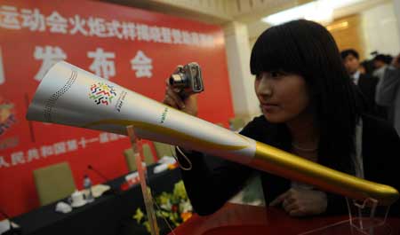 A girl takes photos of the torch named 'Ruyi' for China's 11th National Games in Jinan, capital of east China's Shandong Province, April 28, 2009. Using the image of Chinese traditional ruyi, an s-shaped ornamental object which is usually made of jade and is a symbol of good luck, the torch made a debut in Jinan on Tuesday. [Xinhua]