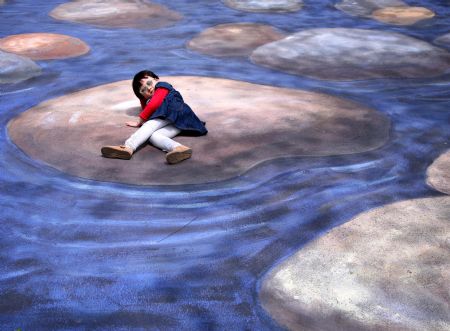 A kid poses for a photo on a cubic drawing displayed at the Xuanwuhu Park in Nanjing, capital of east China&apos;s Jiangsu Province, April 25, 2009. More than 30 such pictures are displayed here recently, a strong cubic effect of which can be seen from a certain angle. [Xinhua/Wang Xin] 