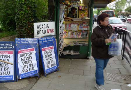 A pedestrian walks past placards of swine flu news at a newsstand in London, the United Kingdom, April 28, 2009. 