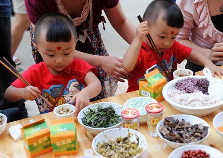 A pair of young twins enjoy the feast during the 5th twin festival in the Hani Autonomous County of Mojiang, southwest China's Yunnan Province, May 2, 2009. A traditional Hani nationality feast on 2-kilometer-long table was held here on Saturday during the three-day twin festival with participation of nearly 1,000 pairs of twins and triplets. (Xinhua/Lin Yiguang)