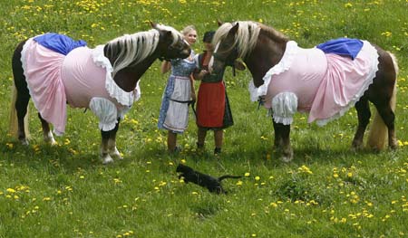 A cat jumps in front of Cosima Scheiding (L) and Monika Kappl holding two horses dressed in a traditional Bavarian Dirndl costume in the eastern Bavarian village of Kirchberg im Wald, May 5, 2009. Bavarian designer Hildegard Bergbauer, who creates Dirndl dresses for women, also makes and sells Dirndl outfits for home pets and horses.