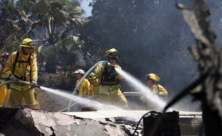 Firefighters spray water on the rubble of a house that burned during the Jesusita fire in Santa Barbara, California May 7, 2009. An out-of-control, wind-driven wildfire bore down on Santa Barbara on Wednesday, destroying some 20 homes in the rugged central California foothills, forcing thousands of residents to evacuate and injuring three firefighters.