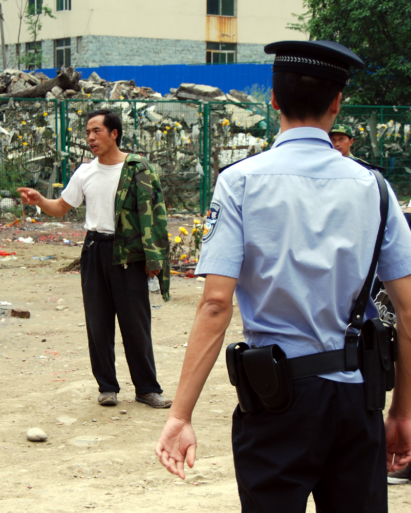 A bereaved parent shouts his anger outside Beichuan Middle School as a police officer looks on. [John Sexton/China.org.cn]