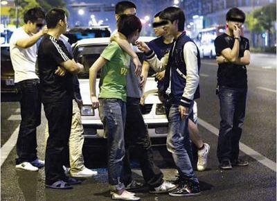 The photo taken on May 7, 2009 shows the two friends who raced with Hu Bin kidding with others as if nothing had happened, when they visited the scene after the accident. The young men, stood around, smoking and chatting, are believed to be from rich families. [Photo: Guangzhou Daily]