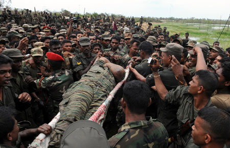 The body of Liberation Tigers of Tamil Eelam (LTTE) leader Vellupillai Prabhakaran is carried on a stretcher through a group of Sri Lankan soldiers at Nanthikadal lagoon, near the town of Mullaittivu in northern Sri Lanka May 19, 2009. Sri Lanka's army chief said Tamil Tiger leader Prabhakaran's body was found on Tuesday, and Sri Lankan TV stations aired video of what appeared to be his corpse, with the top of its head blown off. [China Daily/Agencies] 