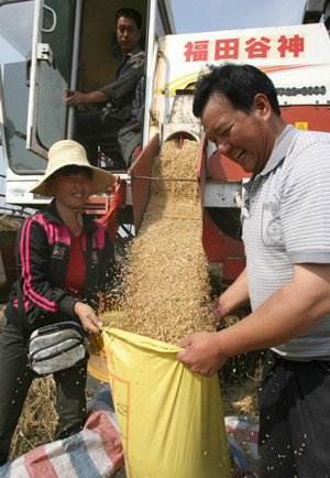 Two local villagers grin while bagging in wheat kernels poured down from the combined harvester, at Yanhu District, Yuncheng City, north China's Shanxi Province, May 21, 2009. [Xue Jun/Xinhua]