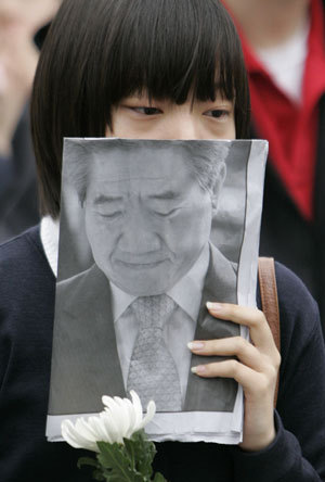 A weeping student holds a flower and an extra edition of a local newspaper as people wait their turn to offer incense for deceased former South Korean President Roh Moo-hyun at a temporary memorial altar arranged by citizens on a street in central Seoul May 23, 2009.(