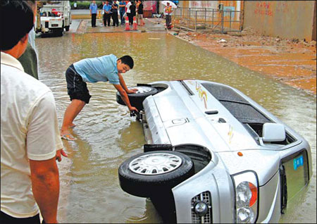 A man checks a minivan which capsized in a pit of water formed after days of heavy rain in Shenzhen on Sunday. The driver and two passengers escaped. [Xu Wenge/China Daily] 