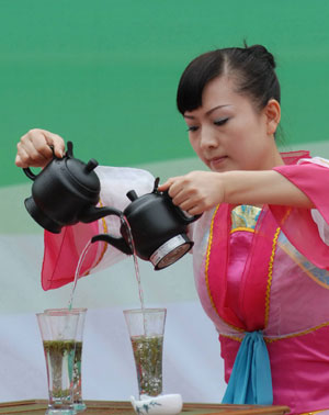 A girl shows her skill of cross-arm pouring water into the tea cups at the opening ceremony of the Enjoying Fragrant Tea with Health in Guiyang, southwest China's Guizhou Province, May 26, 2009. The 5-day activity will feature art performance related to tea culture.